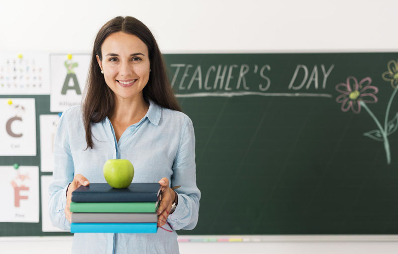 smiley teacher holding a bunch of books and an apple with copy space