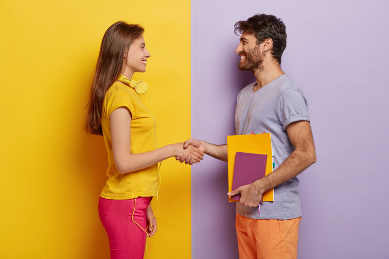 happy groupmates meet after holidays shake hands agree to work together as team stand in profile lovely woman with headphones meets friend unshaven young man holds notepad talks with female
