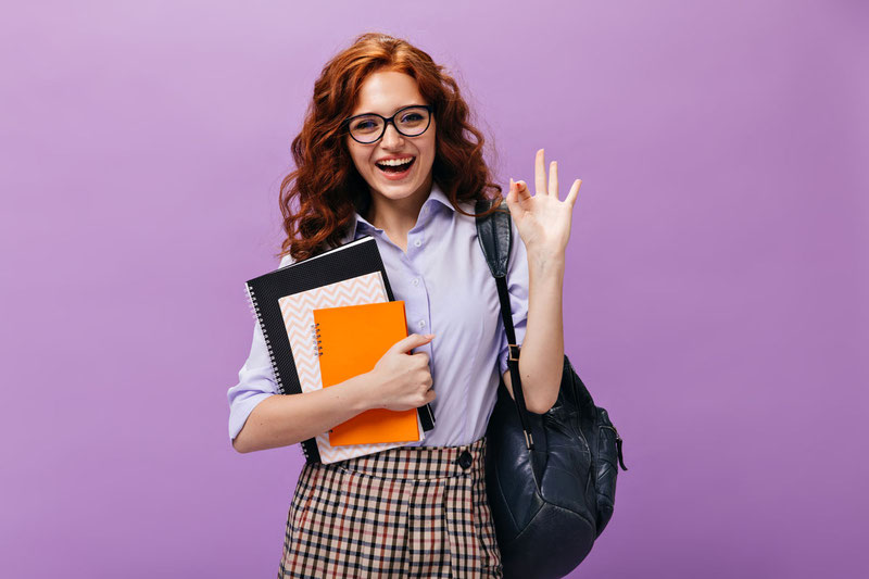 red haired lady eyeglasses holds books shows ok sign