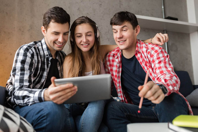 happy young people looking in tablet students learning having fun friends party at home hipster company together two men one woman smiling positive online education using device 1